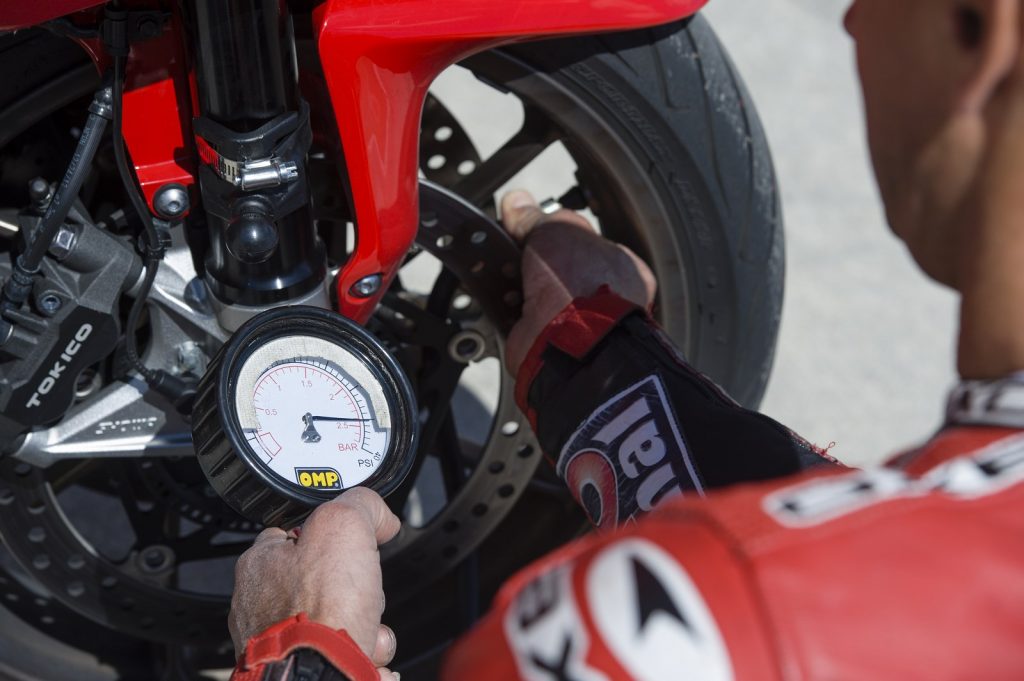 Un pilote qui vérifie la pression de son pneu de moto avec un manomètre