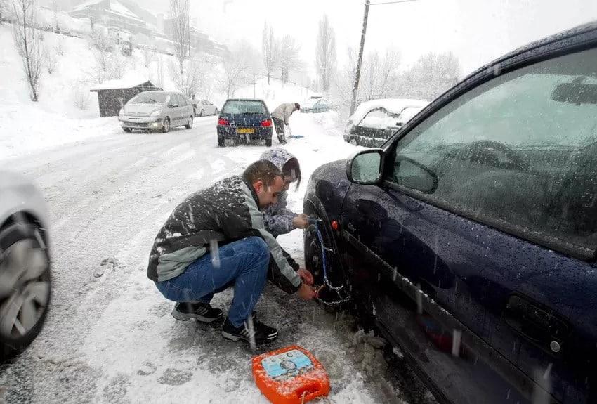 Un automobiliste monte des chaines sur sa voiture bloquée dans la neige